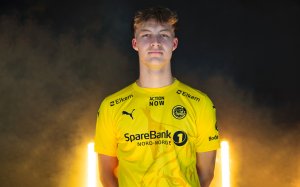 Villads Nielsen poserer i Glimt-drakt etter at han signerte for Bodø/Glimt. I bakgrunnen ser vi gule lys og røyk. 