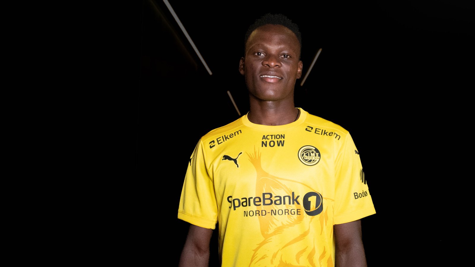 Gift Sunday har signert for Bodø/Glimt og poserer i den gule Glimt-drakta i et mørkt rom der bare han er opplyst