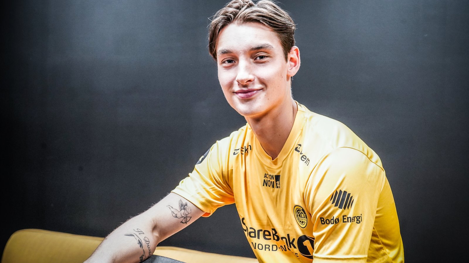 Glimt-spiller Syver Skeide poserer sittende med Glimt-drakt og et smil om munnen fra den dagen han signerte for klubben i 2023