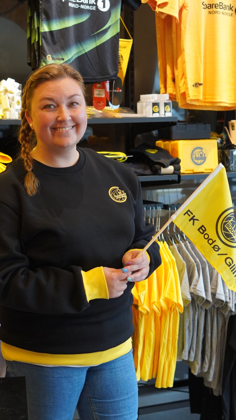 Butikksjef i Glimt-shop, Catrhine Jakobsen, viser frem håndflagget som før ble produsert med plasthåndtak, men som nå produseres i tre. Akkurat for å vare lengre.